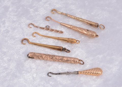 Seven unmarked yellow and gilt metal button hooks