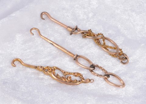 Three ornate yellow and gilt metal button hooks